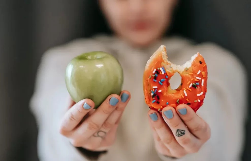 A woman holding an apple and a donut 